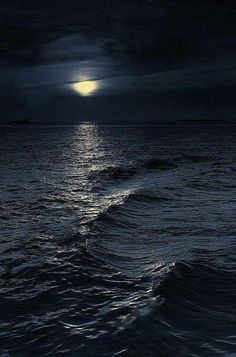 the moon is setting over the ocean on a dark night with waves crashing in front of it