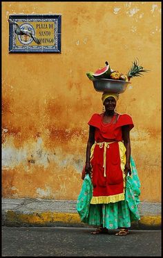 a woman with a bowl on her head standing in front of a yellow and orange wall