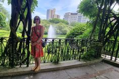 a woman standing in front of a fountain with trees and buildings in the back ground