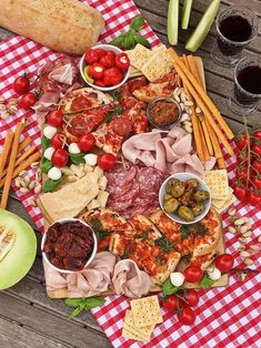 an assortment of meats and cheeses on a picnic table with tomatoes, olives, bread