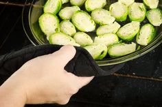 a person is holding a black glove in front of an oven filled with cooked brussel sprouts