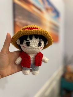 a small crocheted doll wearing a straw hat and red scarf is held up to the camera