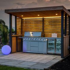 an outdoor bbq with grill and lights on the outside patio at night, in front of a wooden fence