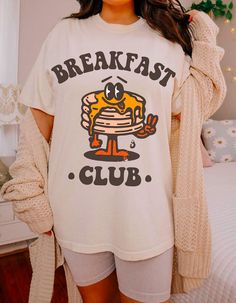 Embrace the joy of mornings with our 'Breakfast Club' tee, where comfort meets whimsy! Crafted from soft, cozy fabric, this shirt features an adorable stack of pancakes, complete with a buttery grin that'll brighten your day. Perfect for lazy brunches or just lounging around, it's a deliciously delightful addition to your wardrobe. Join the club and spread the pancake happiness everywhere you go! Cozy Cotton T-shirt With Graphic Print, Cotton T-shirt With Letter Print For Brunch, Cozy White Graphic Print T-shirt, Cute Crew Neck Tops For Brunch, White Crew Neck T-shirt For Brunch, Funny Print Cotton Tops For Brunch, Graphic Tee With Letter Print For Brunch, Cotton Graphic Print T-shirt For Brunch, Cotton Top With Funny Print For Brunch