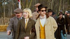 two people walking down the street with other people in coats and hats behind them,