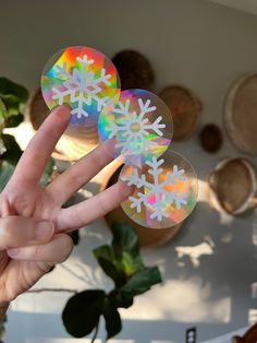 someone holding up two stickers with snowflakes on them in front of a plant