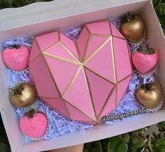 a pink heart shaped cake in a box surrounded by gold apples and strawberries on the side