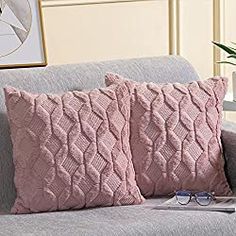 two pink pillows sitting on top of a gray couch next to a book and glasses