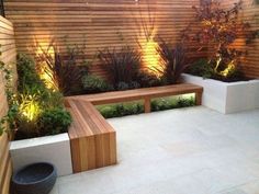 a wooden bench sitting in the middle of a garden next to a wall with lights on it