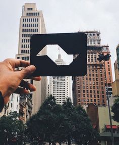 a person holding up a cutout in the middle of a city with tall buildings