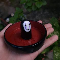 a hand holding a red bowl with a black and white face painted on the inside