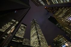 looking up at skyscrapers in the city at night with lights on and street signs below