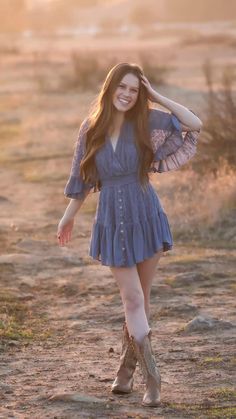 a woman in a blue dress and cowboy boots poses for the camera with her hands on her head