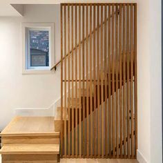 a wooden stair case next to a window in a room with white walls and hardwood floors