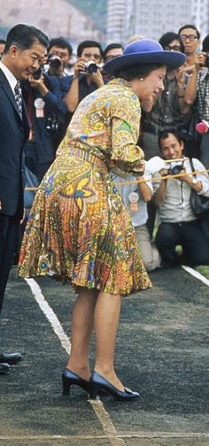 a woman in a colorful dress and hat standing next to a man wearing a suit