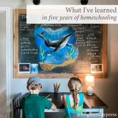 two children sitting at a desk in front of a chalkboard with dolphins on it