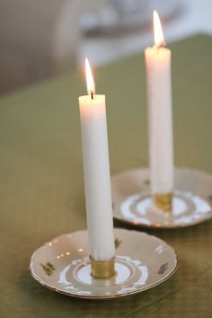 two white candles sitting on top of plates