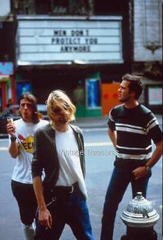 three people walking down the street with a fire hydrant in front of them and a movie marquee behind them