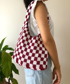 a woman carrying a red and white crocheted bag next to a potted plant