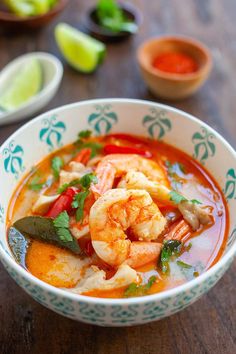 a bowl filled with shrimp and vegetables on top of a wooden table next to limes