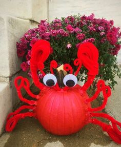 a pumpkin with googly eyes sitting on the ground next to some flowers and bushes