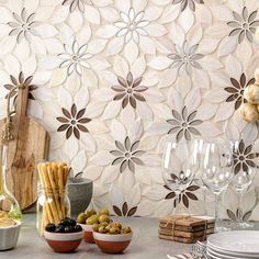 the table is set with wine glasses, plates and utensils in front of a floral wallpaper