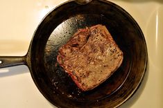 a piece of steak is cooking in a frying pan on the stove top,