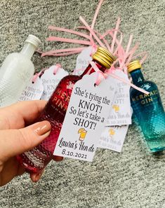 a person holding up a bottle of liquor next to some tags that say she's tying the knott so she takes a shot