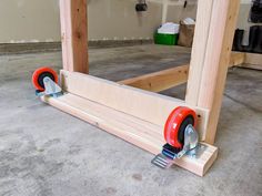 a pair of red wheels are attached to a wooden frame in a garage with other tools on the floor