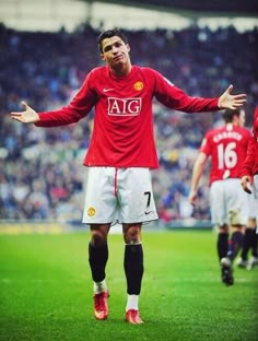 the man is standing on the soccer field with his arms out and two other players are in the background