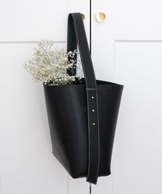 a black leather bag hanging on a white door with flowers in the front and side