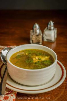 a white bowl filled with soup on top of a wooden table next to silverware