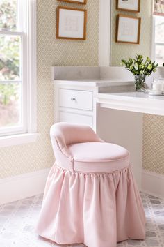 a pink chair with a ruffled skirt sits in front of a vanity and window