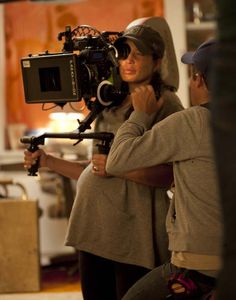 a man and woman standing next to each other in front of a camera set up on a tripod