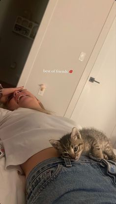 a woman laying on top of a bed next to a kitten