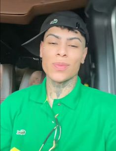 a man in a green shirt and black hat with tattoos on his face is sitting in the back of a car