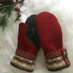 two red mittens sitting on top of snow next to a pine tree with needles