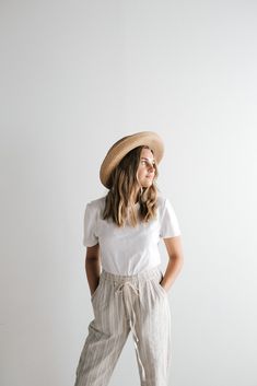 a woman standing in front of a white wall with her hands on her hips wearing a hat