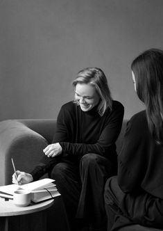 two women are sitting on a couch writing