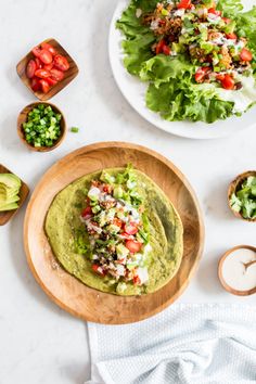 two plates with guacamole, tomatoes and lettuce on them next to bowls of salad