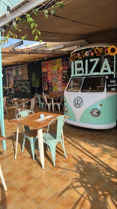 an old vw bus is parked in front of a restaurant with tables and chairs