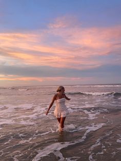 a woman walking into the ocean at sunset