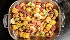 a pan filled with shrimp and corn on the cob next to a lemon wedge