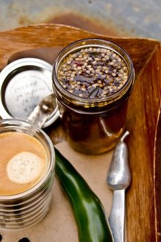 a wooden tray topped with two jars filled with food next to spoons and utensils