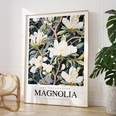 a framed poster with white flowers on it next to a chair and potted plant