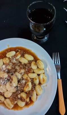 a white plate topped with pasta covered in sauce next to a fork and glass of wine