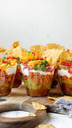 several cups filled with mexican food and chips on a wooden table next to a cutting board