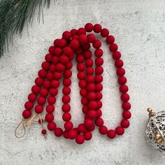 a red beaded necklace next to an ornament on a white surface with pine branches