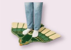 the legs of a person standing on a green and yellow flower shaped floor mat with blue jeans