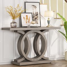 a wooden table with pictures on it in a living room next to stairs and potted plants